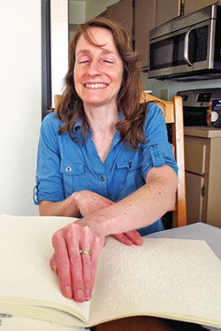 Bridget Bowers, a member of St. Luke the Evangelist Parish in Indianapolis, reads the braille book containing the readings for Sunday Mass at her Indianapolis home on May 15. Bowers receives braille Mass propers from the Xavier Society for the Blind, for which she is now a member of the advisory board. (Photo by Katie Rutter)