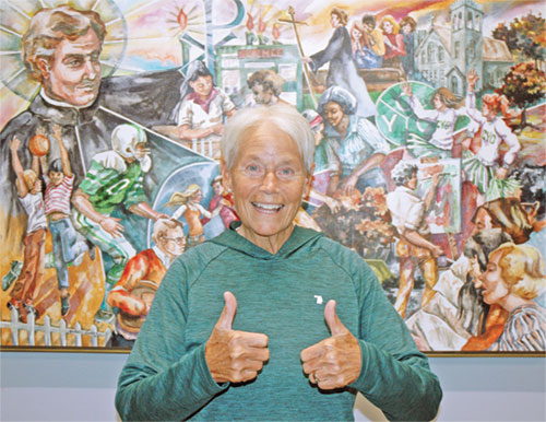 Bernie Price flashes a two thumps-up sign, reflecting how her cancer diagnosis hasn’t diminished her joyful approach to life and her dedication to the archdiocese’s Catholic Youth Organization, which she has served for 51 years. (Photo by John Shaughnessy)